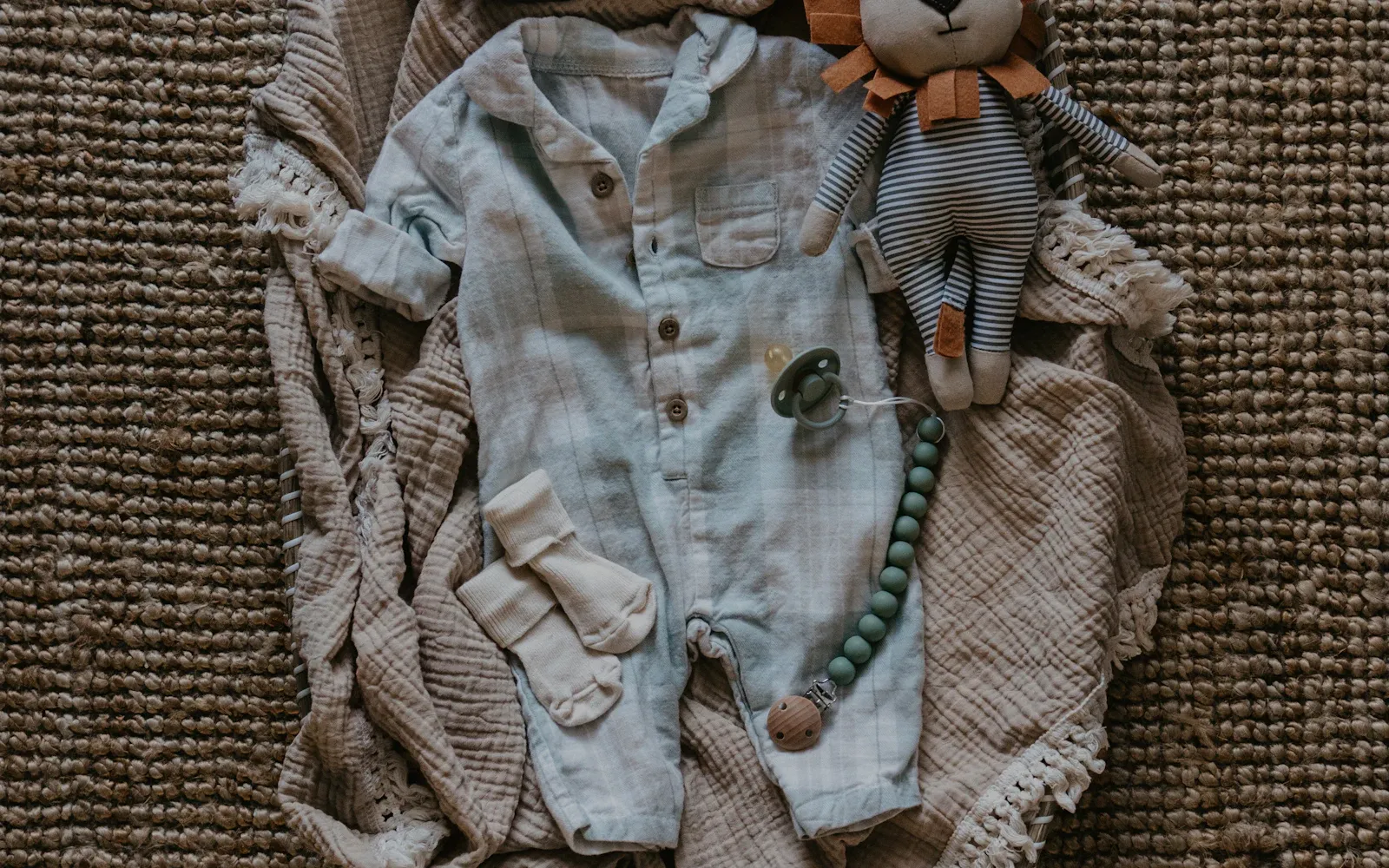 Babystrampler, Söckchen, Kuscheltier und Schnuller auf einer Mulltuch-Decke